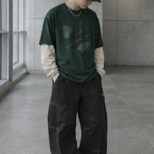 Hombre con camiseta verde oversize streetwear de Urban Mirage, gorra oscura y pantalón baggy negro en un entorno urbano minimalista.