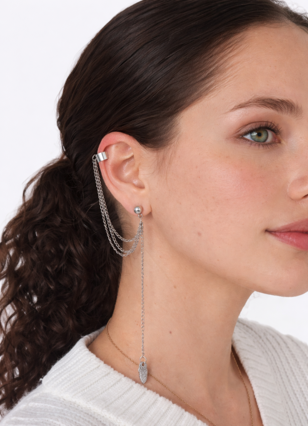 Perfil de mujer joven con coleta rizada y pendientes ear cuff plateados con cadenas de la marca Urban Mirage, estilo streetwear sobre fondo neutro. Imagen generada por IA.