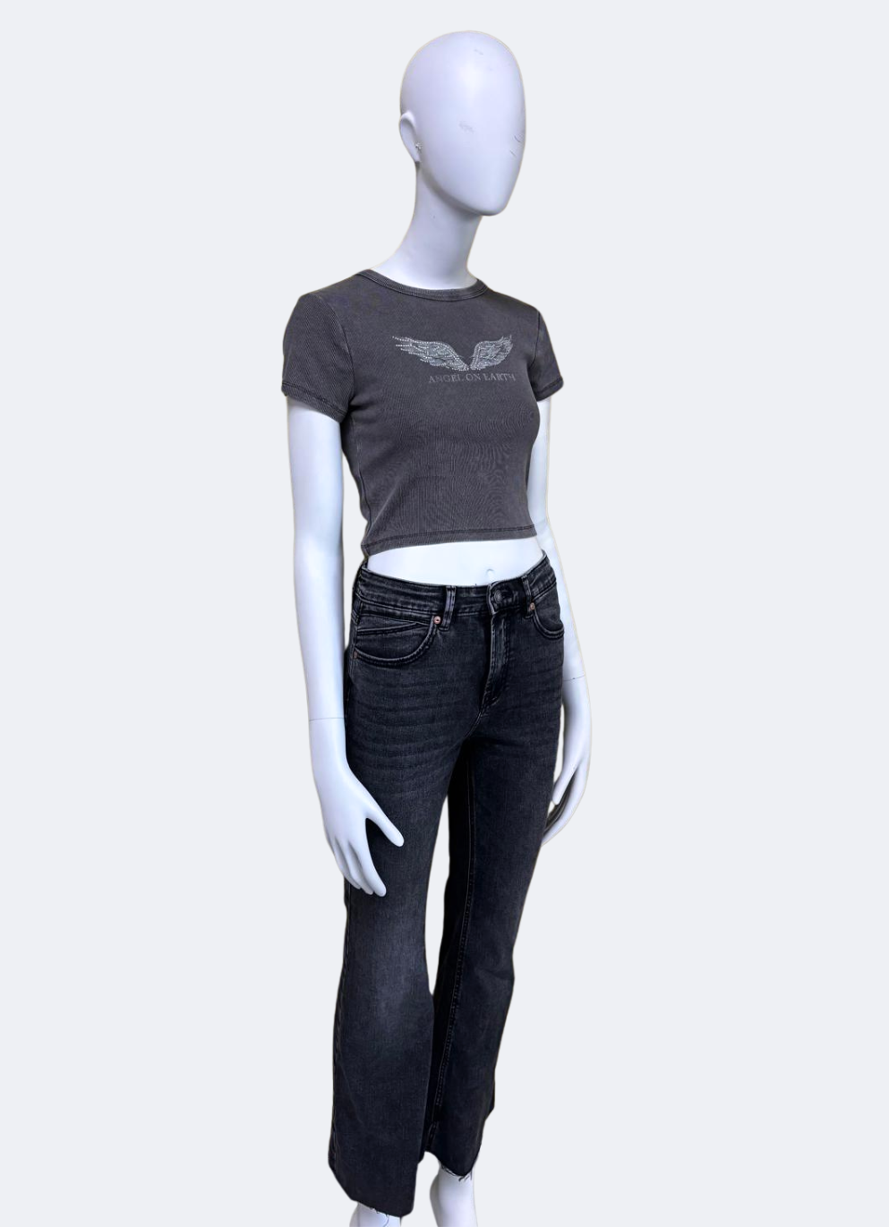 Manequí posando de manera lateral con vaqueros flare negros de tiro medio de la marca Urban Mirage, combinados con camiseta cropped gris. El estilo es casual con acabado moderno y silueta acampanada. Ideal para outfits streetwear.