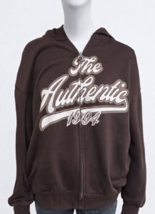 Sudadera streetwear marrón de Urban Mirage. Con estampado frontal "The Authentic 1994" y otro estampado trasero con los carácteres "74" en grande y en más pequeño "Challenge accepted". Tejida de algodón con bolsillos y capucha.